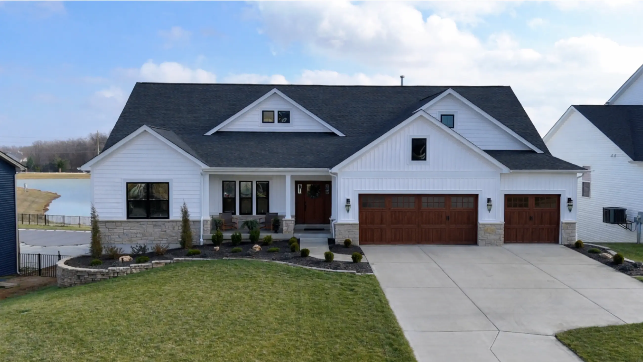 102 Royal Troon, white craftsman ranch with wood-toned garage doors overlooking a lake.